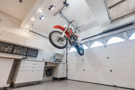 Motorcycle suspended in a clean garage using a bike lift, highlighting organized storage and ample workspace.
